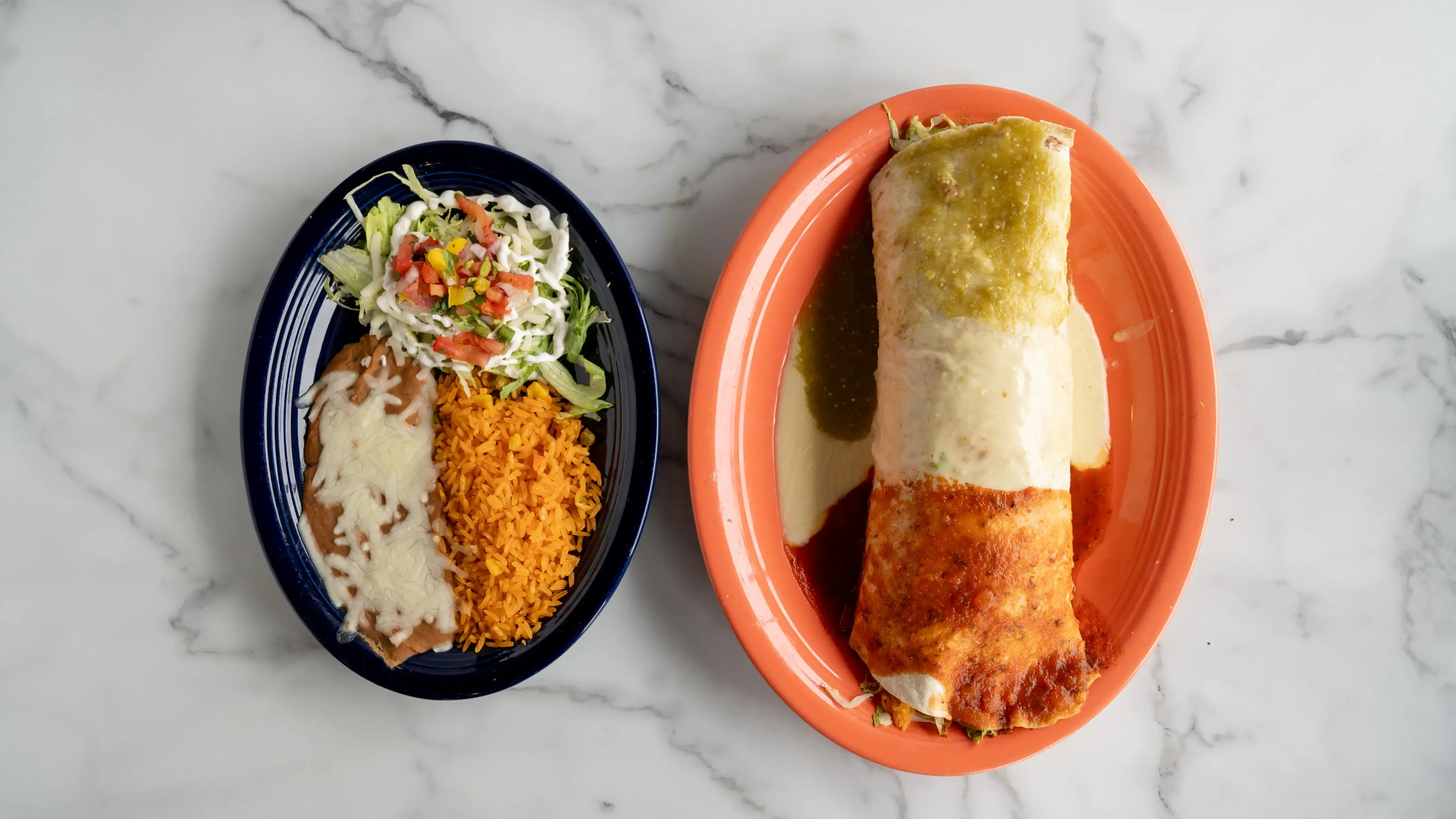 Large Mexican burrito cut in half showing seasoned meat, rice, beans, and fresh toppings
