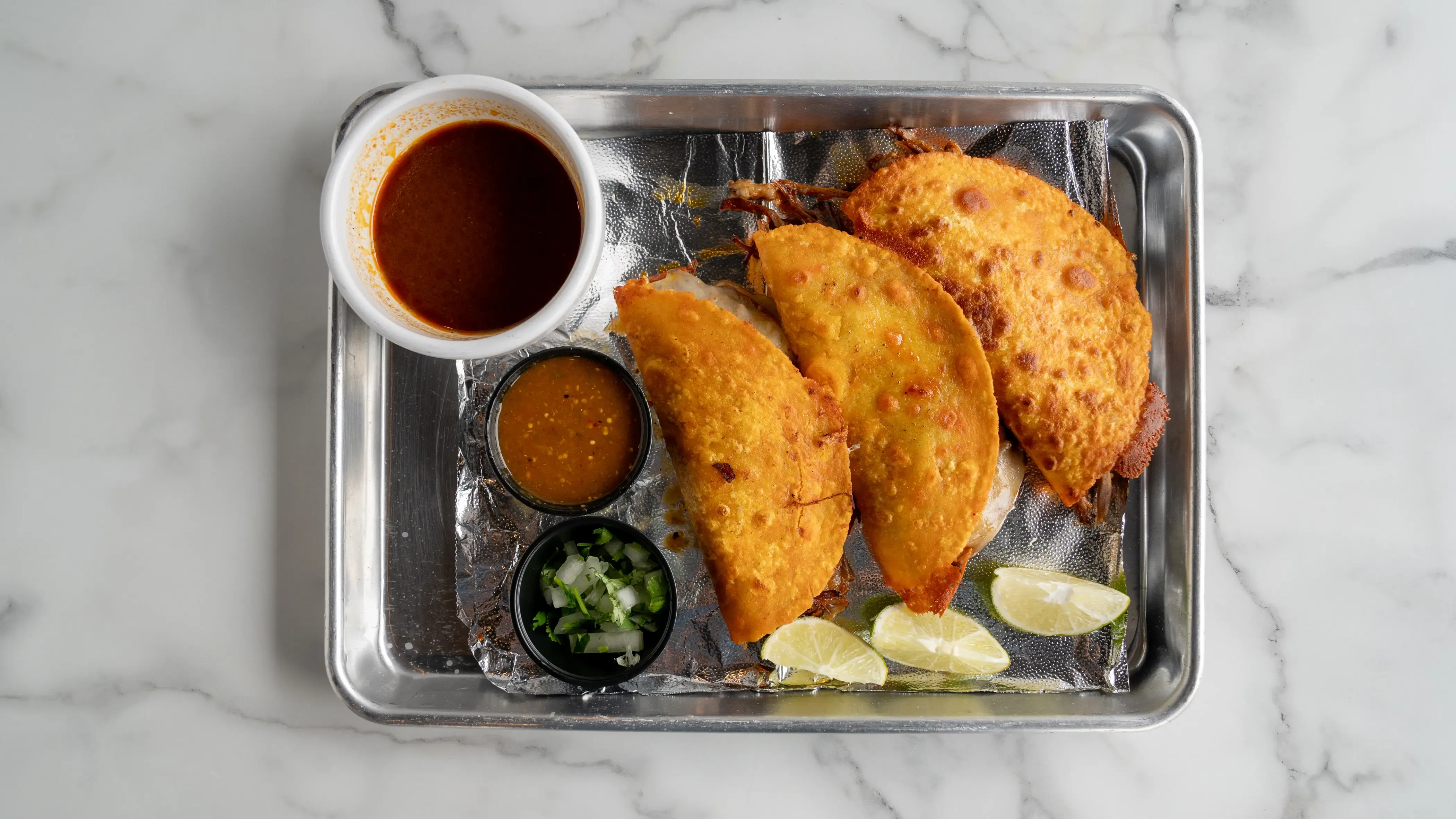 Three authentic Mexican street tacos with carnitas, onions, and cilantro